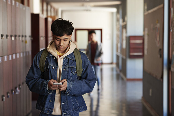 Teenager schaut im Schulflur auf sein Handy