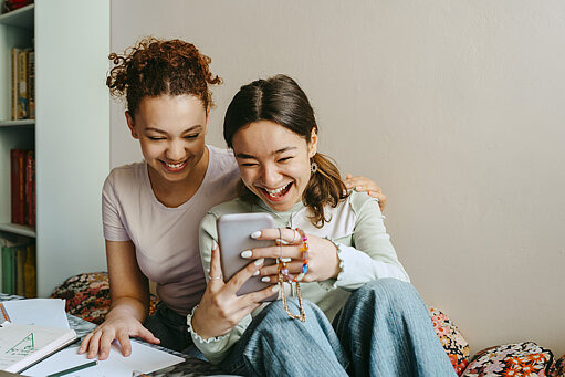 Zwei Teenagerinnen schauen lächelnd auf ein Handy
