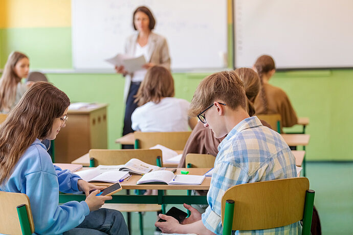 Schülerin und Schüler benutzen ihre Handys unter dem Tisch.