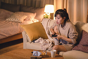 Jugendliche sitzt auf Sofa mit Controller in der Hand