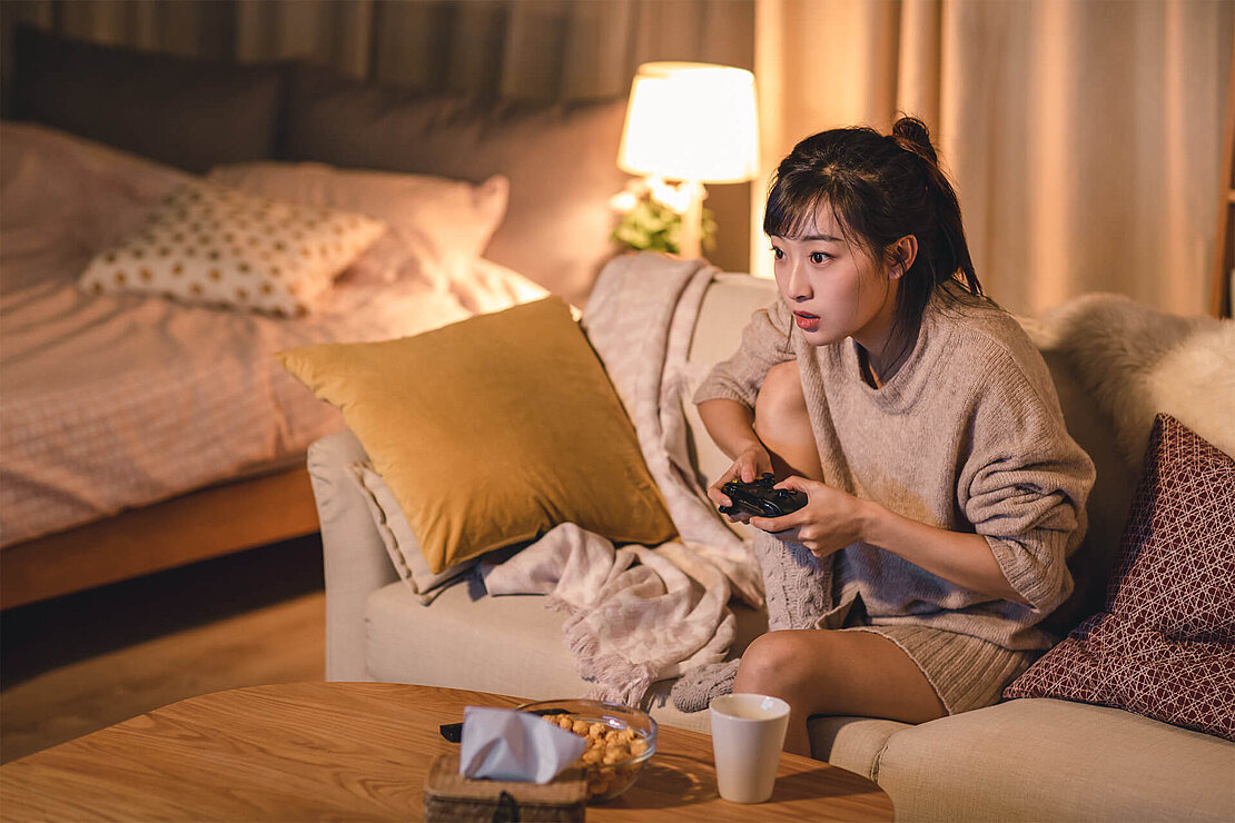 Jugendliche sitzt auf Sofa mit Controller in der Hand