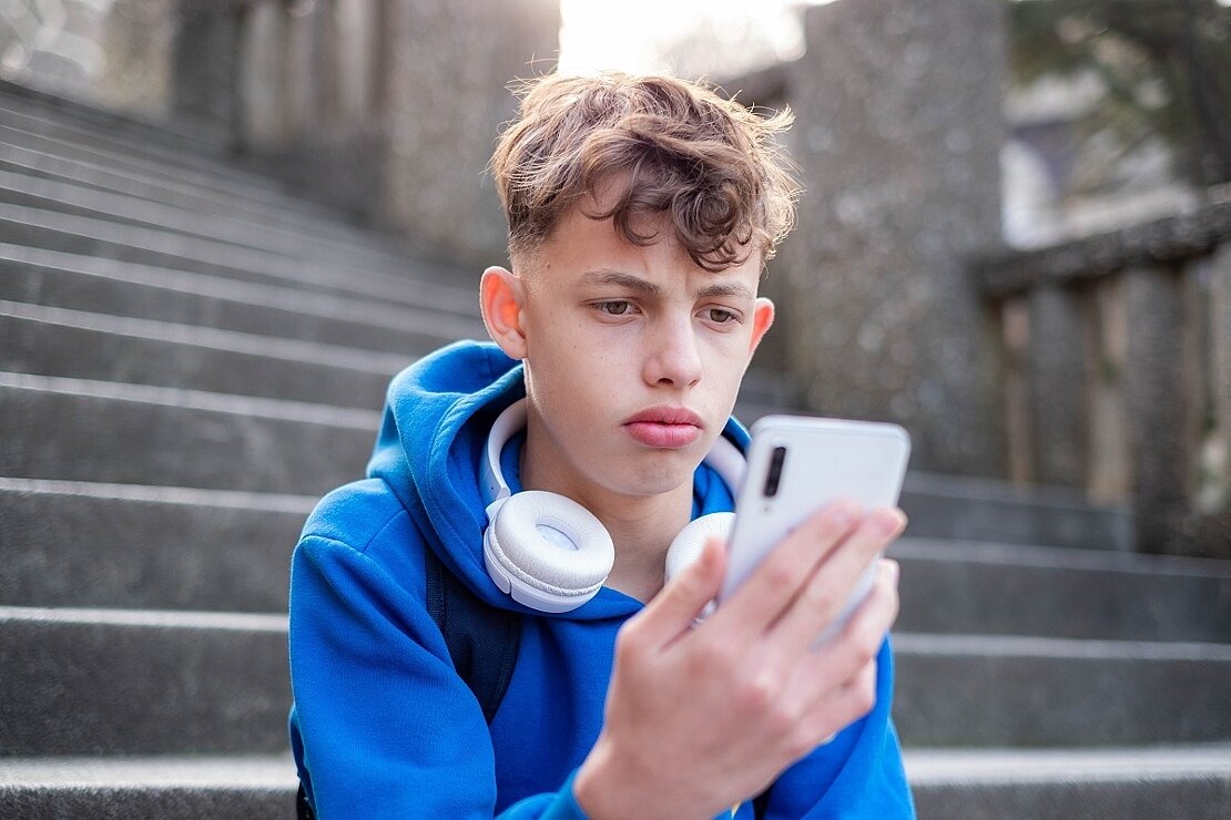 Junge schaut traurig auf Smartphone