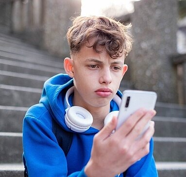 Junge schaut traurig auf Smartphone