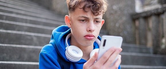 Junge schaut traurig auf Smartphone