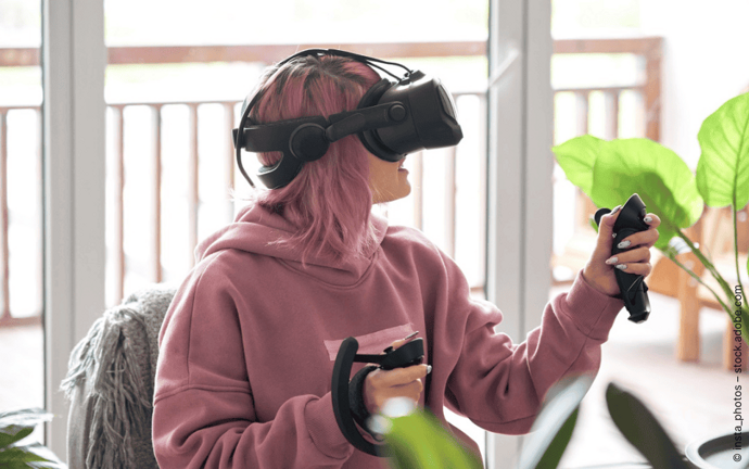 Jugendliche spielt mit VR-Brille und Controllern