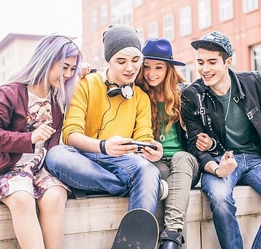 Vier Jugendliche sitzen auf Mauer, schauen auf ein Smartphone
