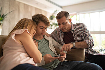 Eltern schauen mit Sohn zusammen auf Smartphone