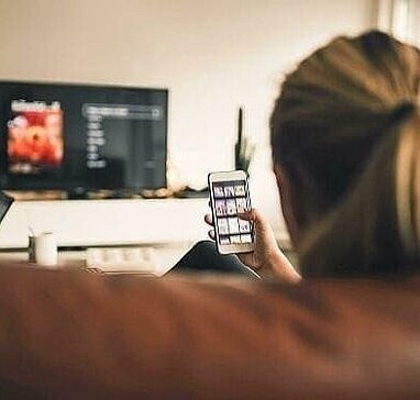 Jugendliche schaut TV und auf Smartphone von Sofa aus