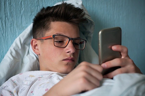 Trauriger Junge liegt im Bett mit Smartphone in der Hand