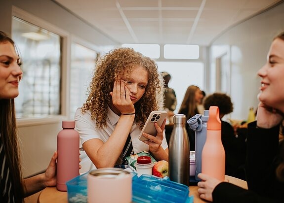 Jugendliche schaut traurig auf Handy während Schulpause