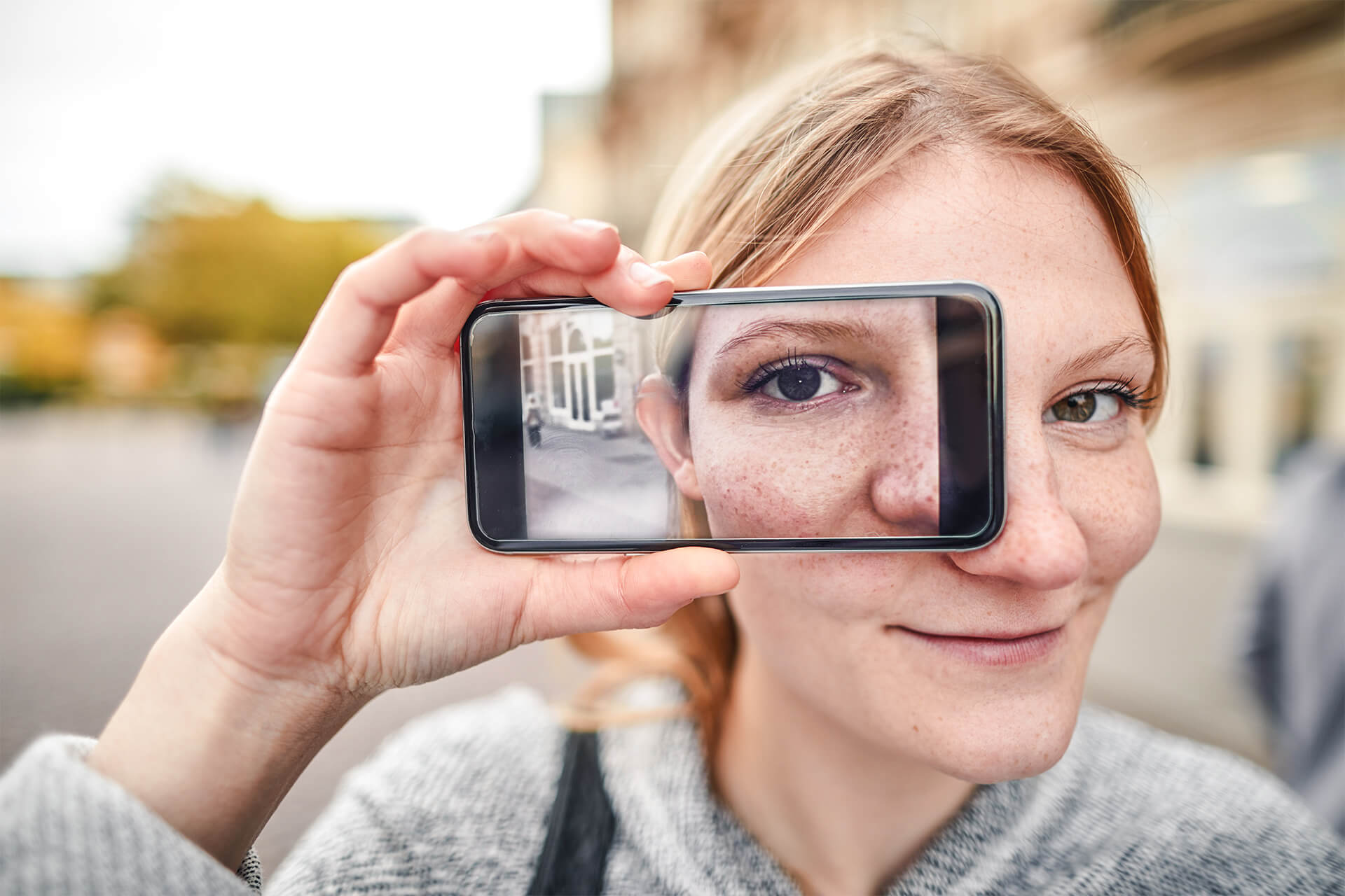 Junge Frau hält sich ihr Handy vor das Gesicht.