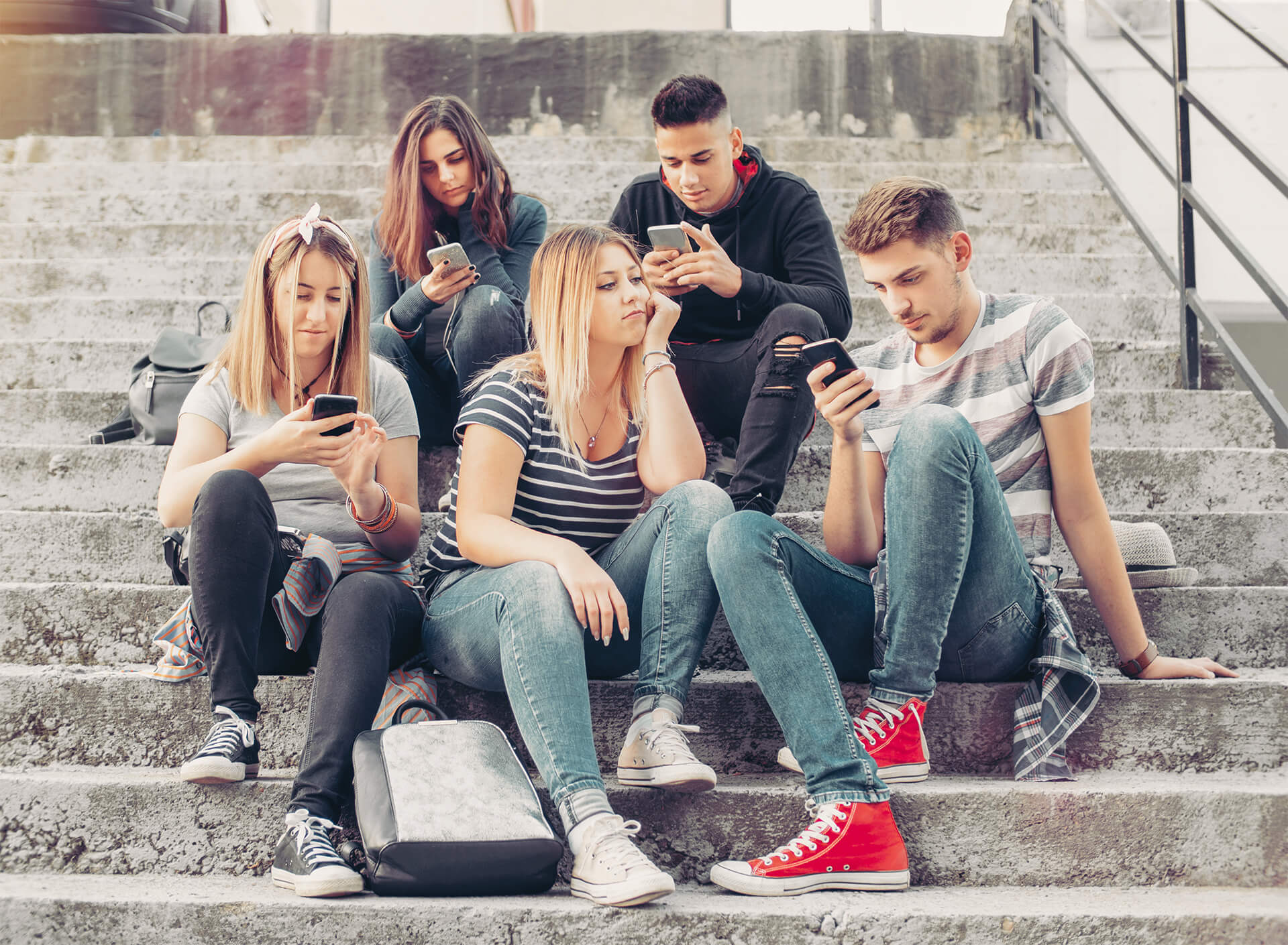 Vier Jugendliche mit Smartphone sitzen auf Treppe, ein Mädchen ohne Smartphone