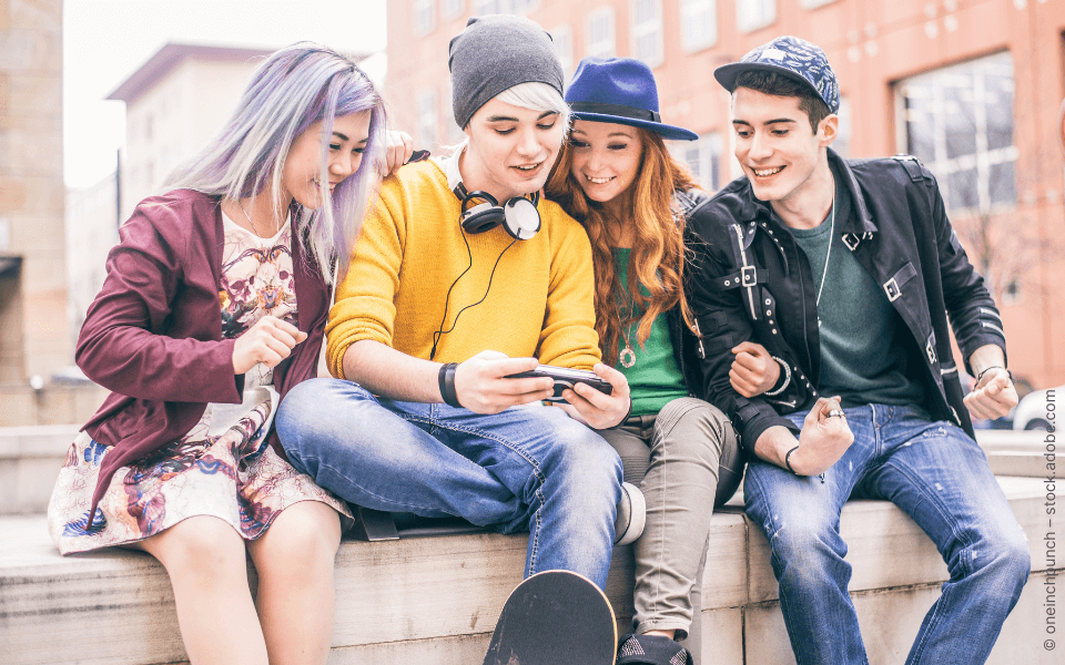 Jugendliche sitzen auf Mauer, schauen auf Smartphone